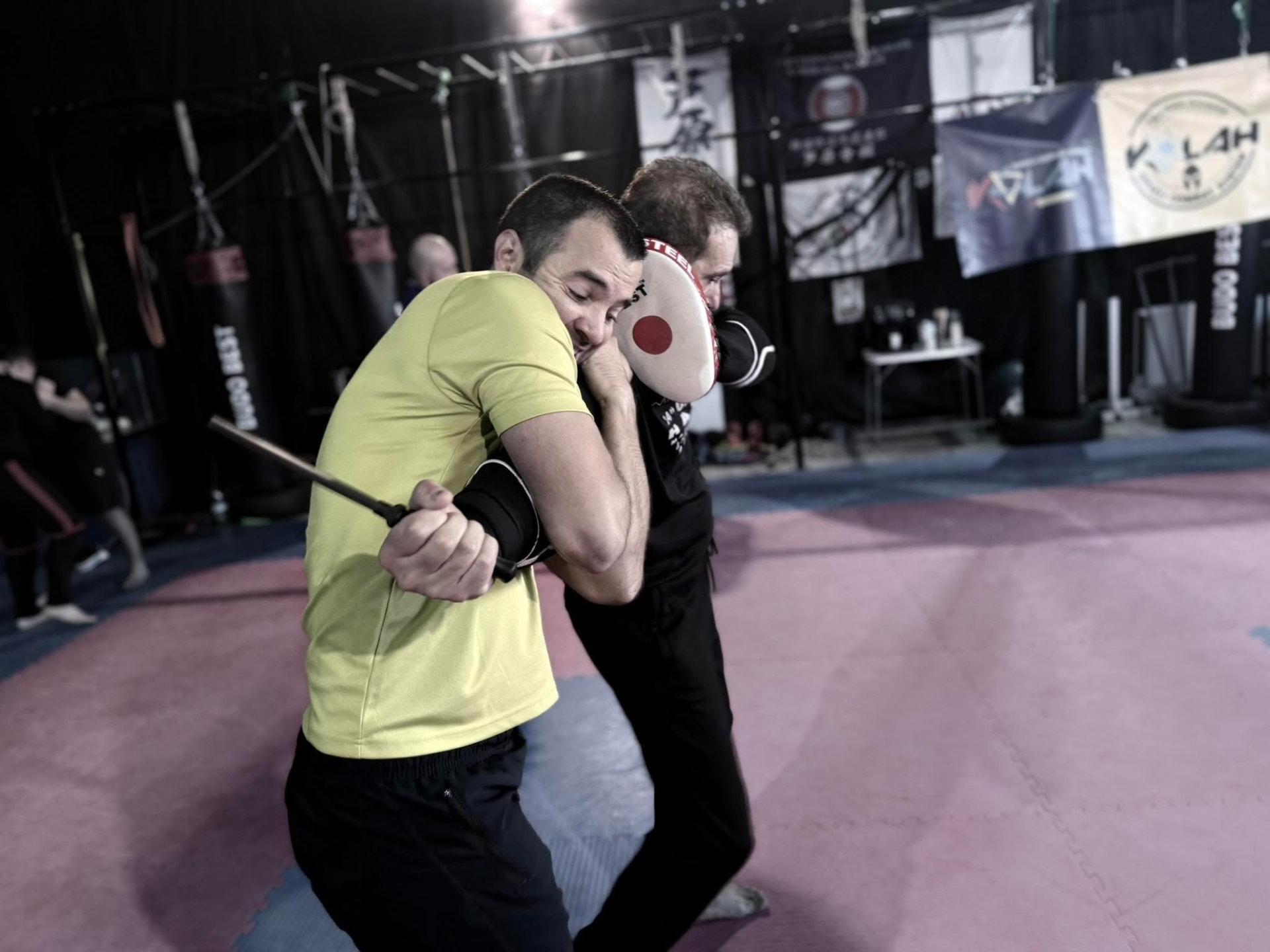 A defender in a yellow shirt controlling the weapon-bearing arm during knife training