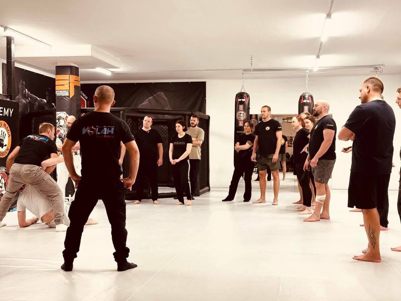A mixed group of adults watching an instructor demonstrate in a Kalah class