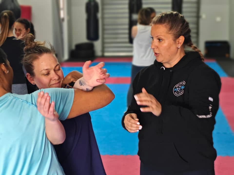 An instructor coaching two women as they practice a defense in class